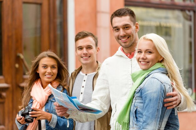 travel, vacation, technology and friendship concept - group of smiling friends with map and photocamera exploring city