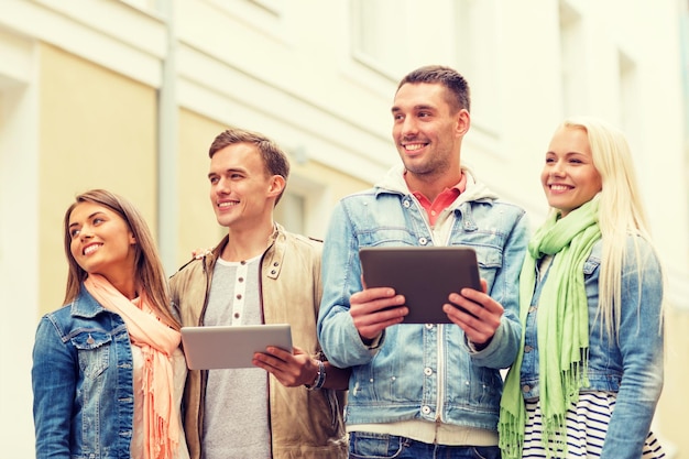 Photo travel, vacation, technology and friendship concept - group of smiling friends with tablet pc computers in the city