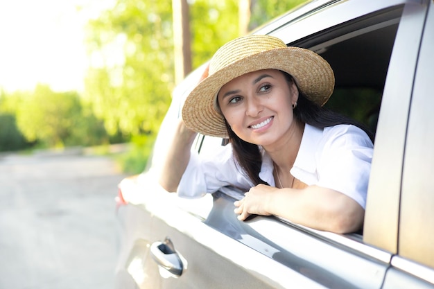 Travel vacation A young beautiful woman in a hat sits in a car and smiles looking into the distance Lifestyle