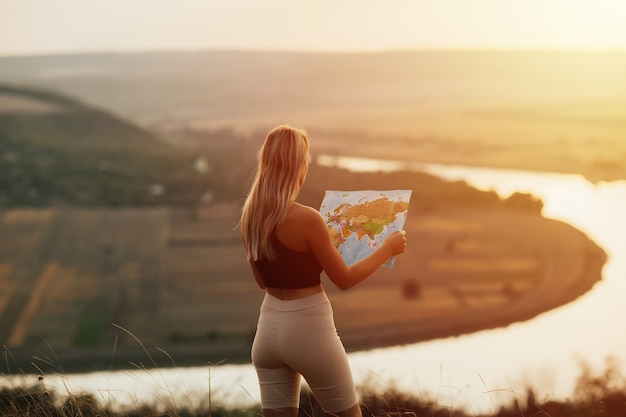 Travel woman reading map at amazing sunset, enjoy the nature landscape. She holding touristic map and planning route in mountains