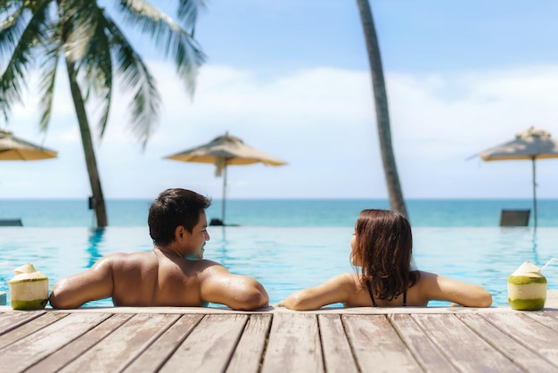 traveler asian couple  with coconut relax in luxury infinity pool hotel resort with sea beach