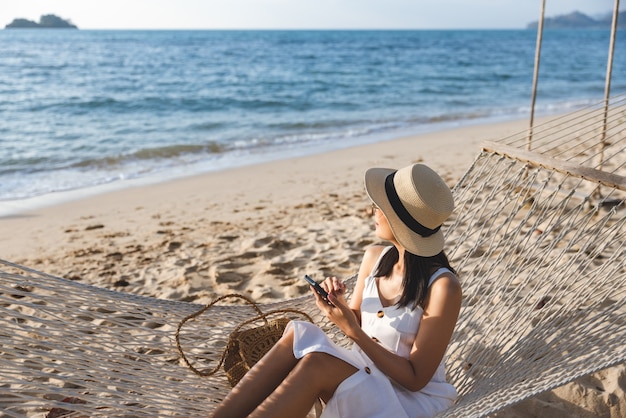 Traveler asian woman using mobile phone and relax in hammock on beach in Koh Chang Trad Thailand