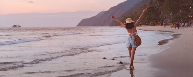 Traveler asian woman with hat relaxing and sightseeing on beach at sunset in Koh Chang, Trat, Thailand