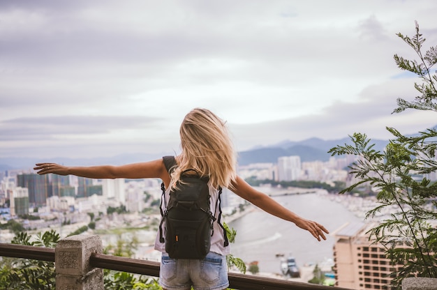 Traveler blonde backpacker woman walking overlooking the downtown. Travel adventure in China, Tourist beautiful destination Asia, Summer holiday vacation trip. Freedom and happy people concept