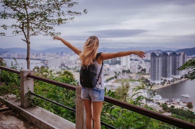 Traveler blonde backpacker woman walking overlooking the downtown. Travel adventure in China, Tourist beautiful destination Asia, Summer holiday vacation trip. Freedom and happy people concept