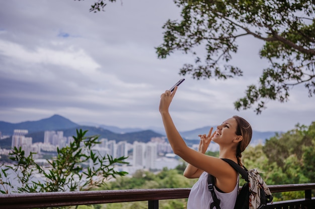 Traveler blonde backpacker woman walking taking photos from observation deck overlooking the downtown. Travel adventure in China, Tourist beautiful destination Asia, Summer holiday vacation trip