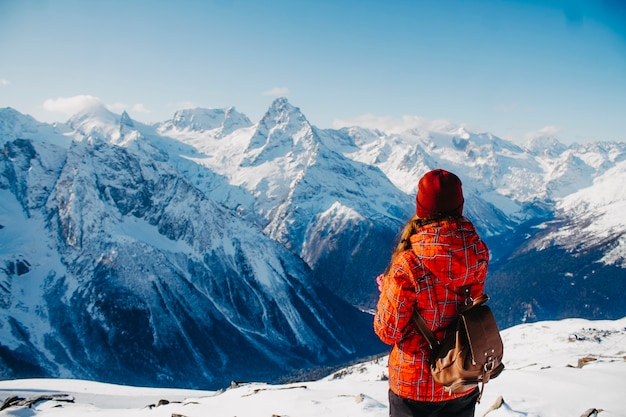 A traveler on the edge of an abyss looks into the distance at the snowy mountains.