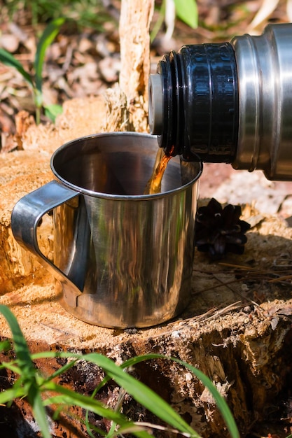 Traveler in the forest pours tea from thermos