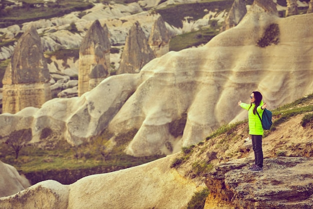 Traveler girl standing on cliff above mountains valley landscape