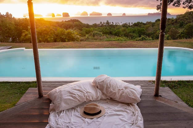 Traveler hat on white bed against Beautiful ocean view background Tourists relaxing in tropical resort with swimming pool travel summer vacation and freelance concept