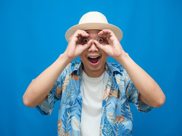 Traveler man wear hat hand circle at his eye blue background