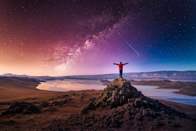 Traveler man wear red clothes and raising arm standing on mountain at with milky way in Lake Baikal Siberia Russia