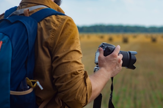 Traveler photographer with a camera in his hand against the background of a field and haystacks.