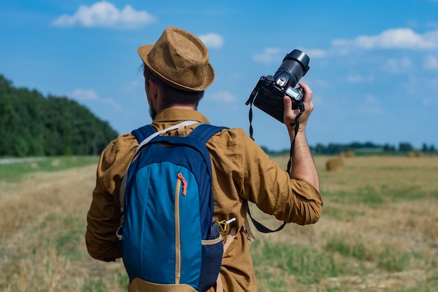 Traveler photographer with a camera in his hand against the background of a field and haystacks.