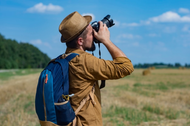 Traveler photographer with a camera in his hand against the background of a field and haystacks.