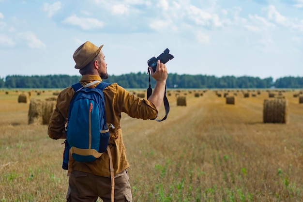 Traveler photographer with a camera in his hand against the background of a field and haystacks