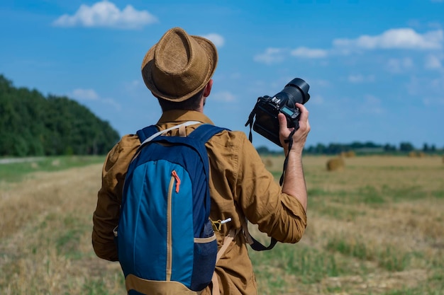 Traveler photographer with a camera in his hand against the background of a field and haystacks