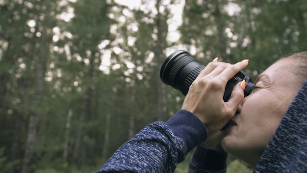 Traveler photographing scenic view in forest One caucasian woman shooting close up look Girl take photo video on dslr mirrorless camera Professional photographer travel with backpack Outdoor