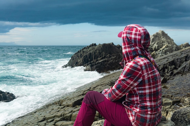 Traveler sits on the shore of a stormy sea on a natural pavement made of columnar granite