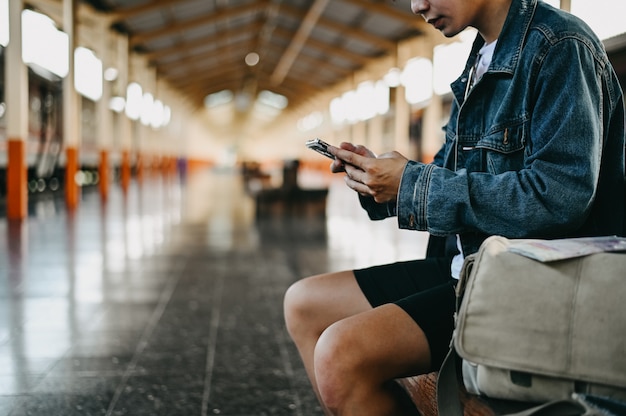 Traveler using mobile phone in train station with backpacker concept.