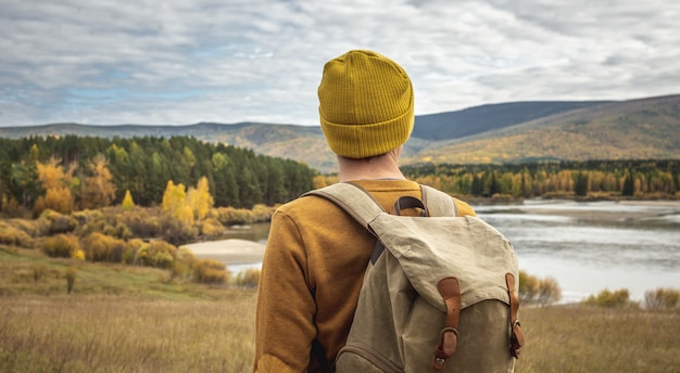 Traveler with a backpack is walking on an empty road along forest. Concept of freedom, travel, hiking and autumn mood