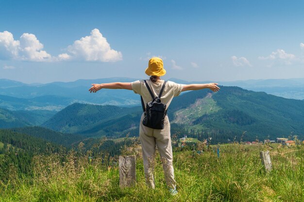 Traveler with a backpack stands with her arms outstretched in the mountains in summer