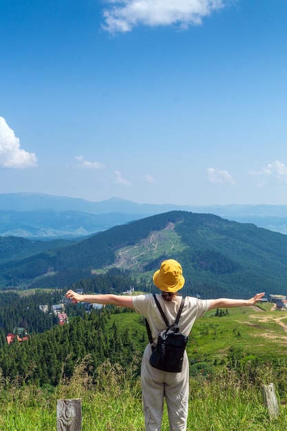 Traveler with a backpack stands with outstretched arms in the mountains in summer