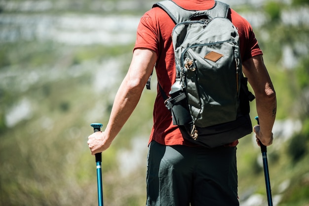 Traveler with backpack and trekking poles in mountainous terrain