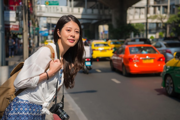 Traveler woman on the road looking for taxi background is urban traffic jam. Asian woman with calling a taxi on bangkok street, thailand.