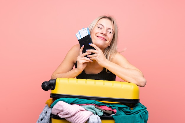 Traveler woman with a suitcase full of clothes over isolated pink wall