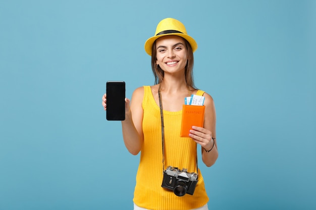 Traveler woman in yellow casual clothes and hat holding tickets, cellphone and camera on blue