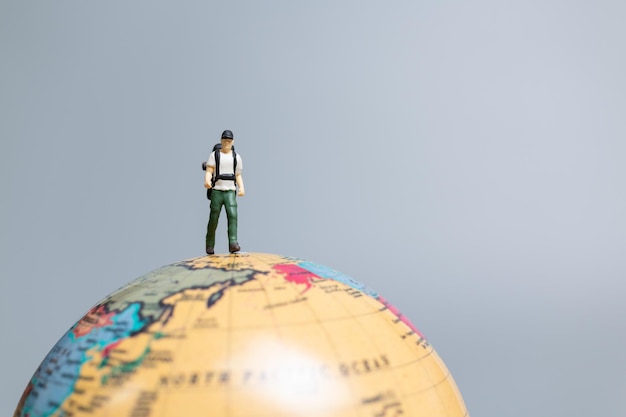 Travelers in miniature standing on the globe and making their way to their destination