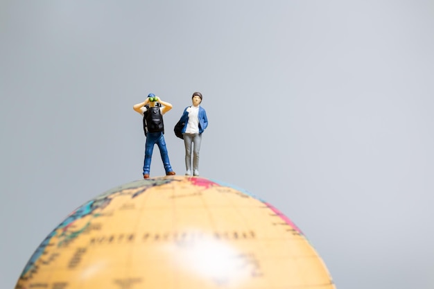 Travelers in miniature standing on the globe and making their way to their destination