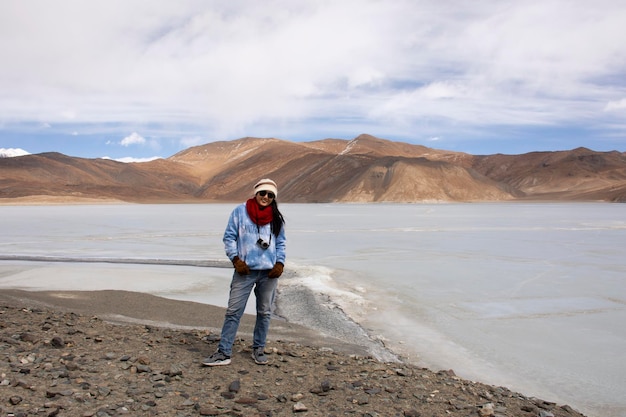 Travelers thai woman travel visit stand for take photo with Himalayas mountains and Pangong Tso high grassland lake while winter season at Leh Ladakh in Jammu and Kashmir India