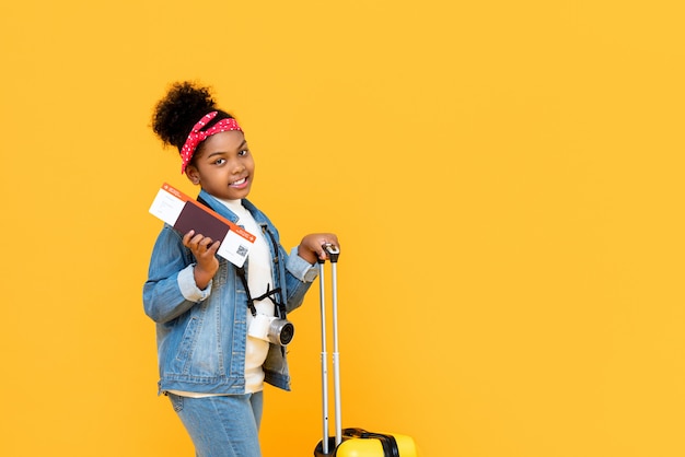 Traveling African American girl wih baggage passport and boarding pass isolated on yellow wall with copy space