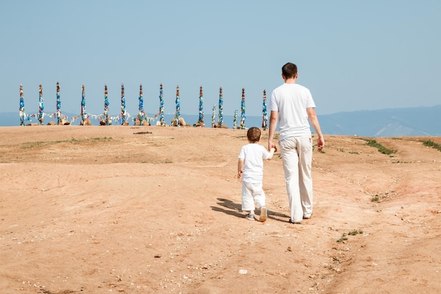 Traveling dad and son walk towards the Sacred pillars with ribbons on the cape of Olkhon Island