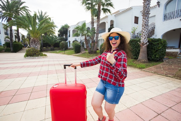 Traveling vacation, holidays, trip and people concept - woman tourist with suitcase showing thumb up