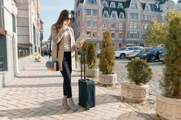 Traveling young woman with mobile phone and suitcase