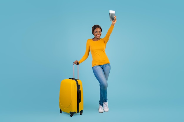 Travelling concept portrait of happy black young woman with suitcase and passport