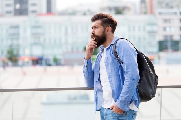 Travelling concept Tourist on vacation Hipster modern tourist urban background Looking for adventures Tourist handsome thoughtful hipster backpack Man with beard and rucksack explore city