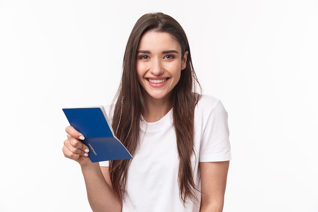 Travelling, holidays, summer concept. Close-up portrait of cute, happy pretty young woman in t-shirt, holding opened passport and smiling