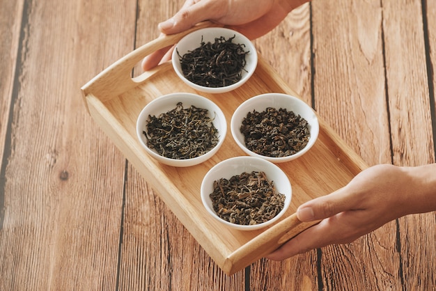 The tray on hands with white bowls of dry teas leaves