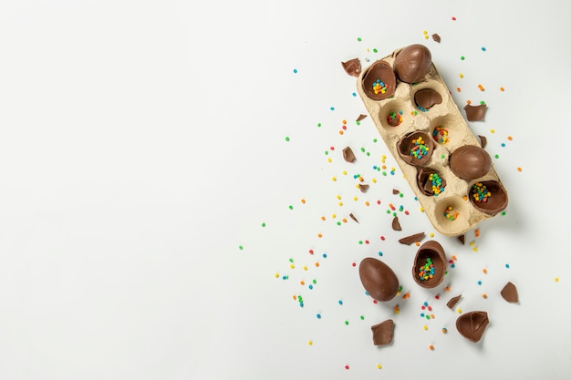 Photo tray with broken easter chocolate eggs and multi-colored sweet candy decorations on a light