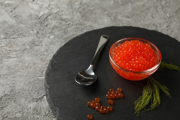 Tray with glass of red caviar, spoon and dill on gray background, space for text