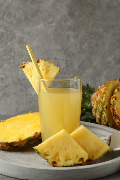 Tray with pineapple slices and glass of juice against gray background