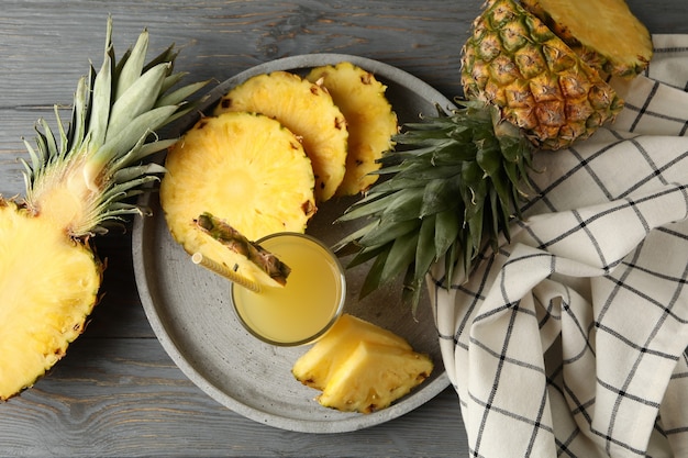 Tray with pineapple slices and glass of juice on wooden background, top view