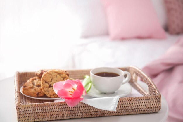 Tray with tasty breakfast and tulip on bed