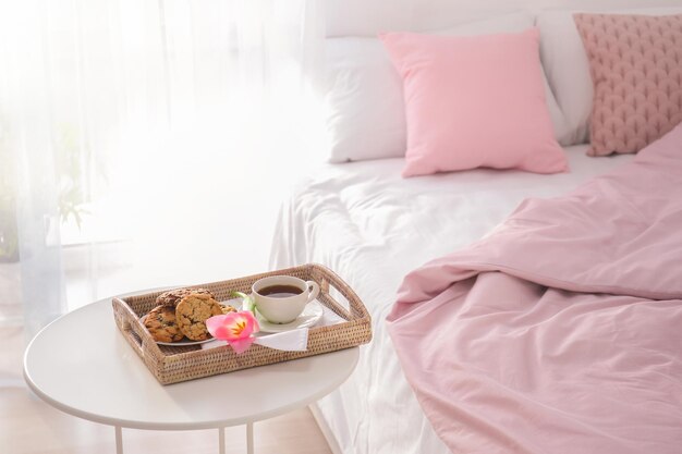 Tray with tasty breakfast and tulip on table near bed