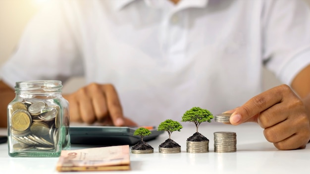 Tree growing on pile of money and businessman holding coins in hand idea to maximize profit from business investment.