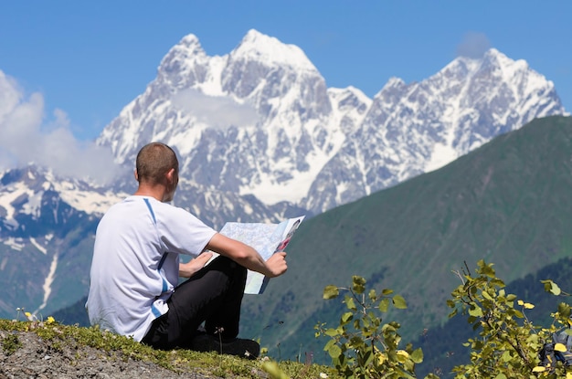 Trekking in the mountains. Tourist checks the route with the map. View of the peak of Ushba. Main Caucasian ridge, Zemo Svaneti, Georgia. World beauty